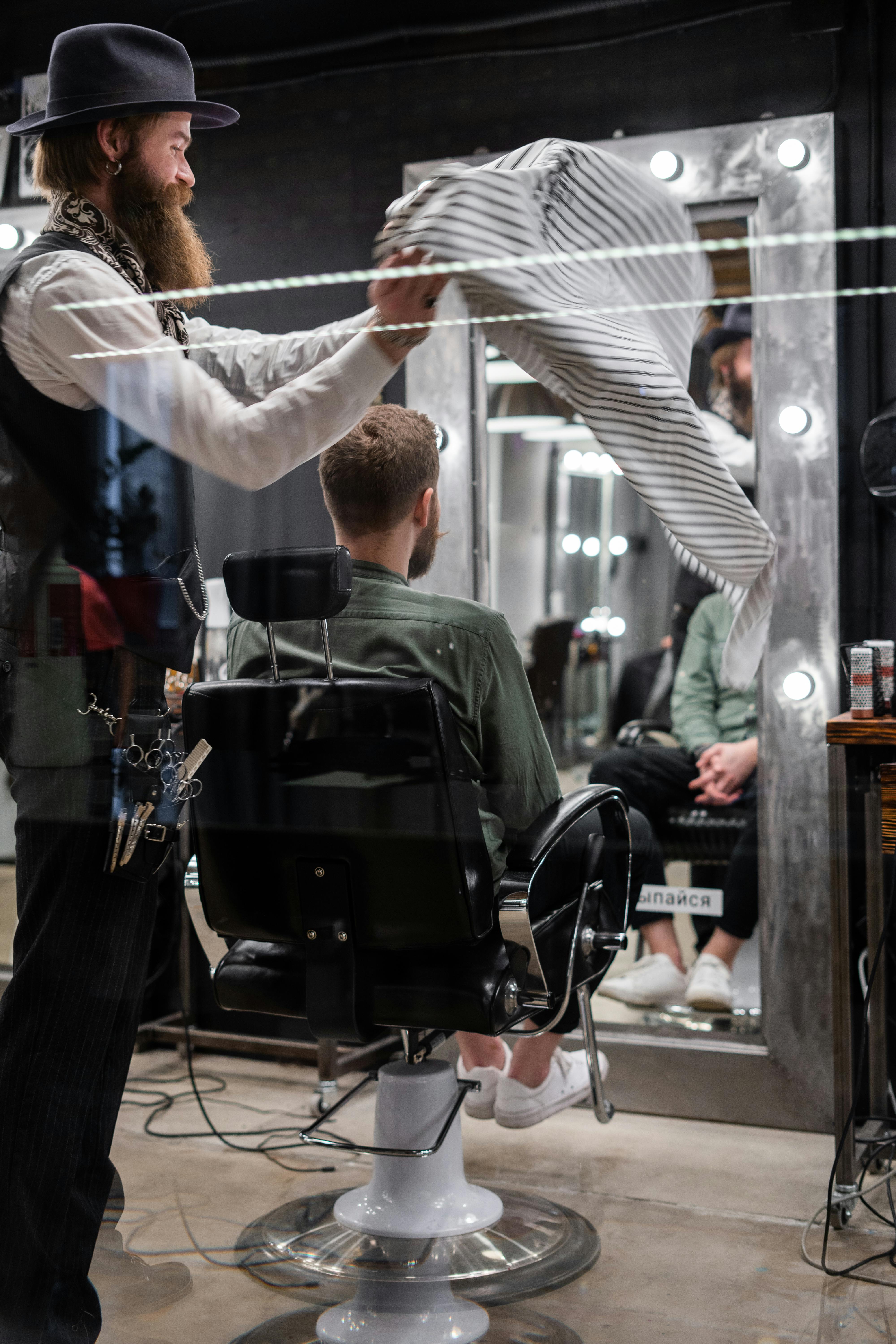 Stylish barber preparing a client in a modern barbershop interior with mirrors and ambient lighting